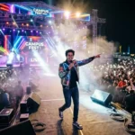 A high-energy college festival stage with professional lighting and students performing, while a student anchor engages the crowd.